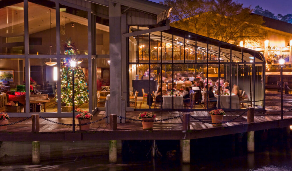 An exterior view of a glass building with people eating and a tall Christmas tree