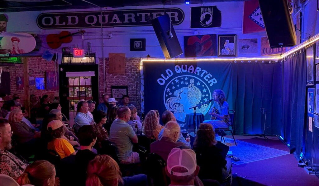 A musician performing on an acoustic guitar in a small venue with a crowd