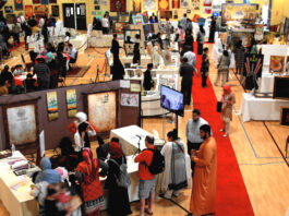 A show floor with artwork stalls and crowds moving between