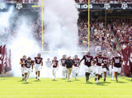 The Texas A&M football squad enters the field flanked by giant maroon flags with smoke behind them
