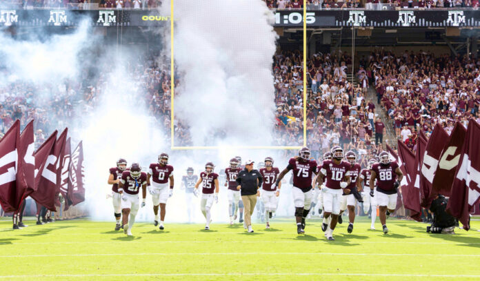 The Texas A&M football squad enters the field flanked by giant maroon flags with smoke behind them