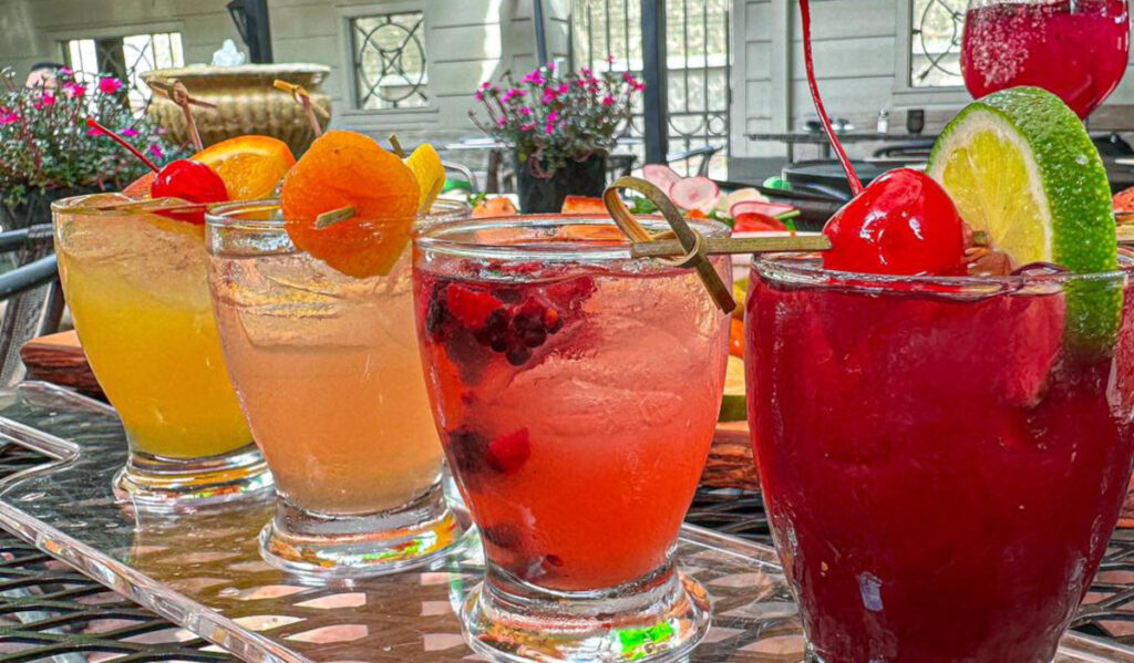 Four colorful cocktails lined up on a table on a patio