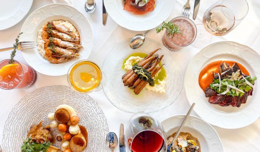 An overhead view of several dishes and drinks on a white tablecloth