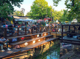 A band performs as a patio of onlookers watch from across a creek