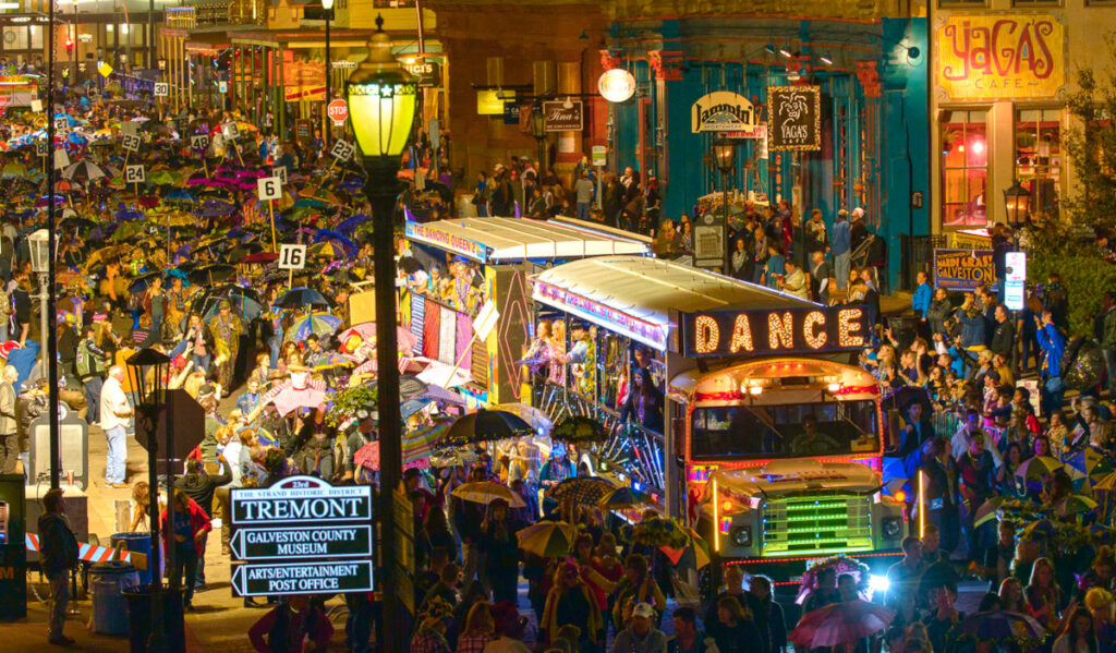 A Mardi Gras parade procession in Galveston led by a bus with a "Dance" banner and crowded by parade revelers