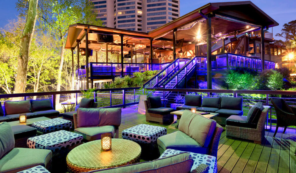 A view from a two-tiered backyard patio of a restaurant with purple lighting at night