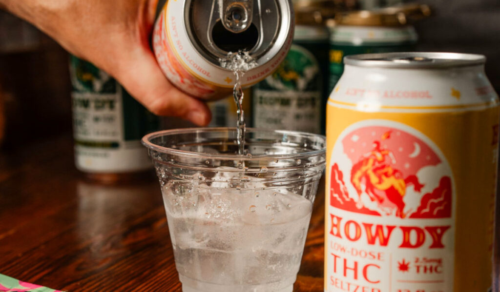 A hand pouring a seltzer into a clear plastic cup next to a can of seltzer