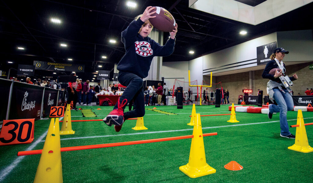 A child running with a football jumps over a set of cones