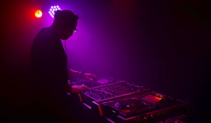 A DJ in silhouette with red and purple lights behind him