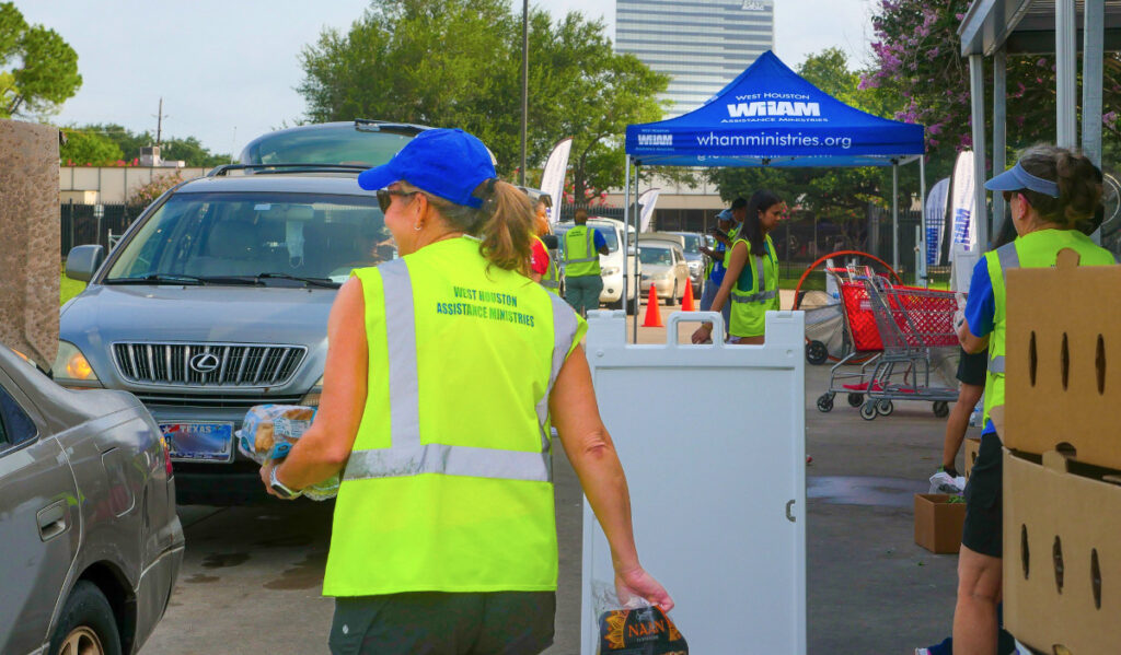 Volunteers in bright yellow jackets bring food to a line of vehicles