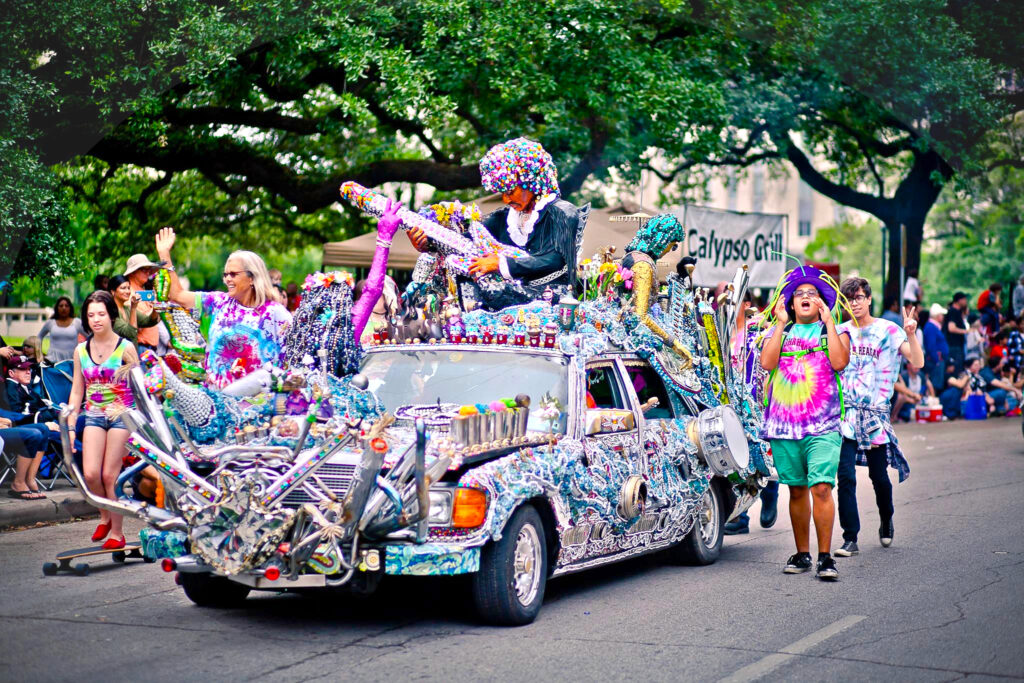 Kids in colorful clothing and hats walk alongside a highly decorative art car