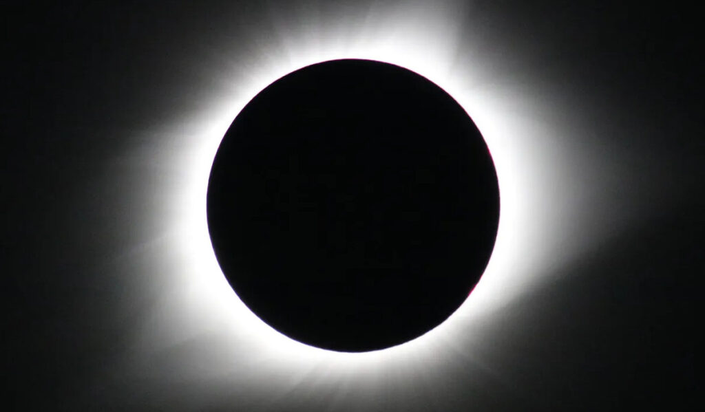 A total eclipse with a white corona around the silhouette of the moon