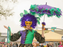 A stilt walker in Mardi Gras costume with a mask and umbrella