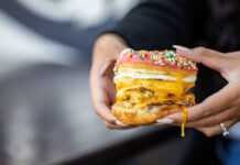 Where to Brunch in The Woodlands Two hands holding a burger with a donut as buns, and egg yolk dripping off a finger