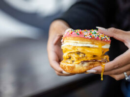 Two hands holding a burger with a donut as buns, and egg yolk dripping off a finger