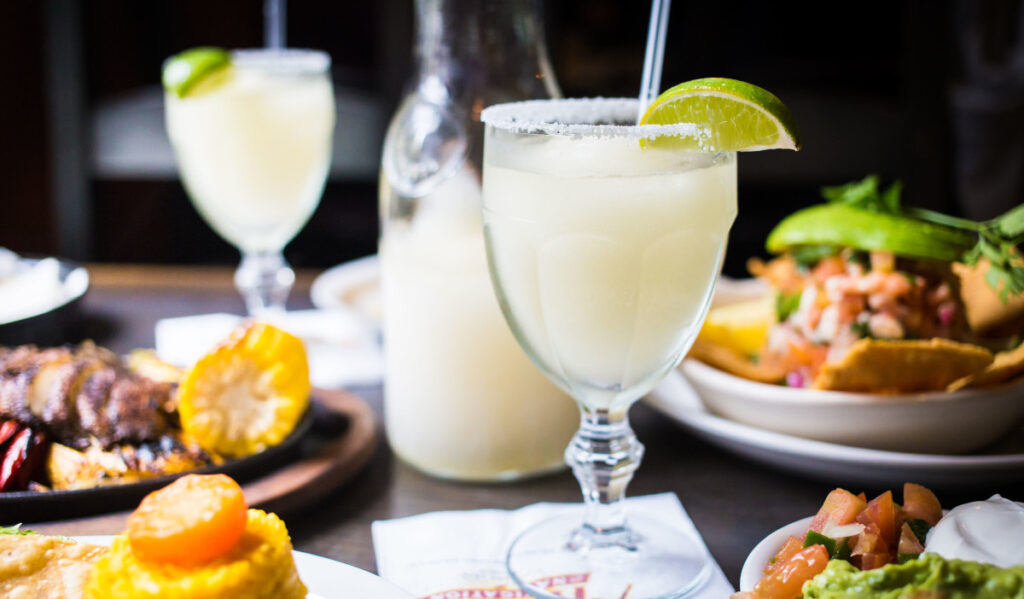 A margarita in a glass with a lime slice on the rim and Tex-Mex food around the glass