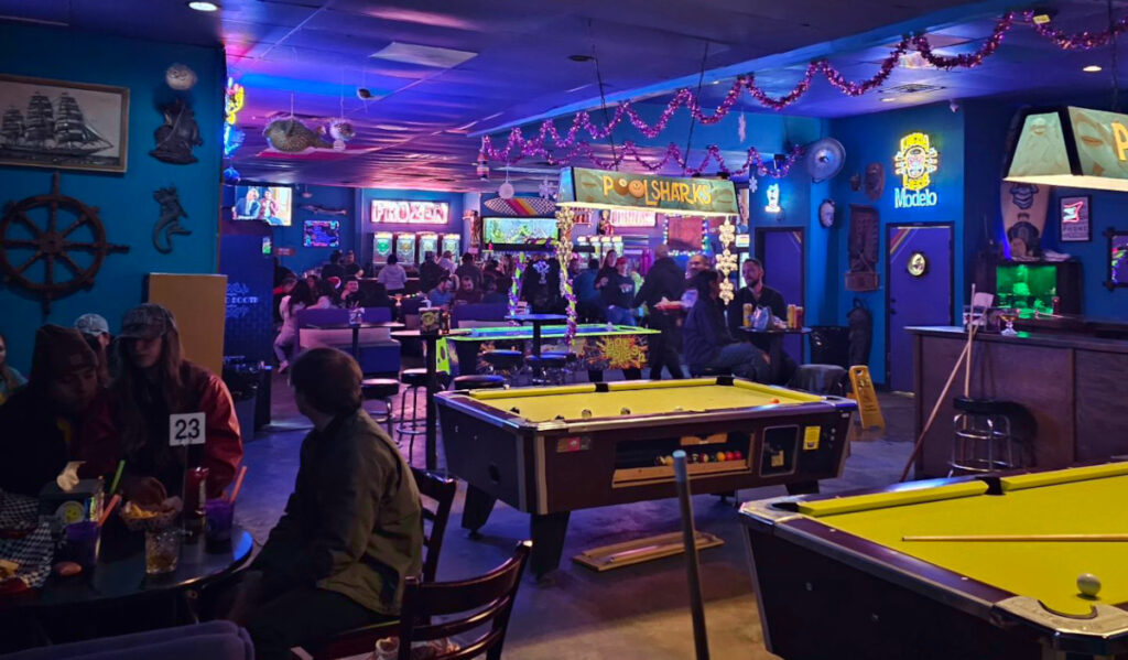 A purple-lit bar interior with pool tables, air hockey and a bar in the distance