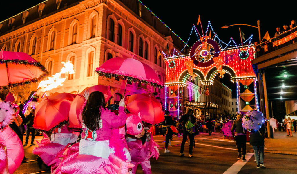 Parade revelers in pink with umbrellas marching toward a lit-up archway