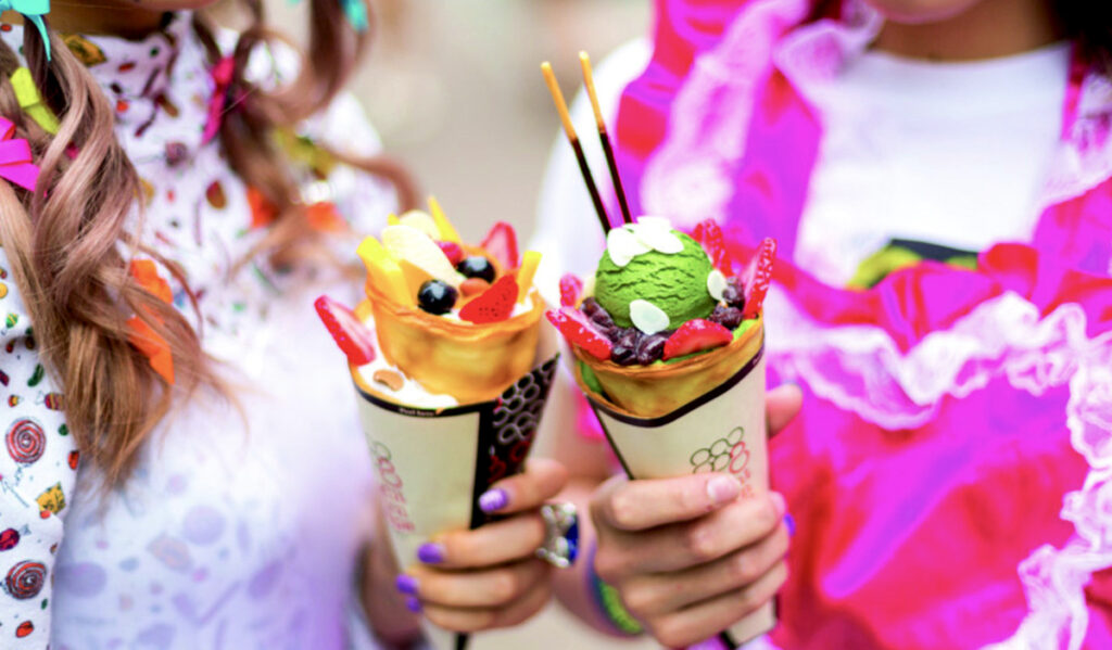 Two people holding cones with ice cream, fruit and other toppings