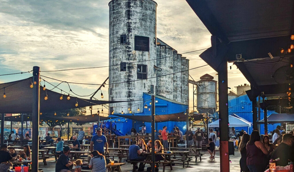 People drinking at tables with an old silo looming over the patio
