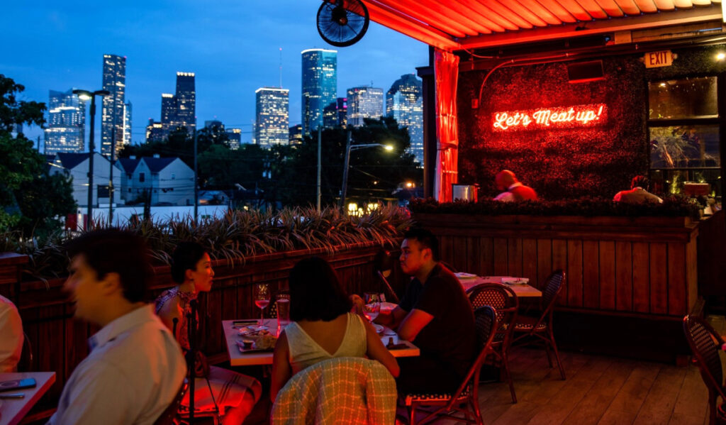 Diners eat on the upstairs patio of a restaurant, overlooking the Downtown skyline