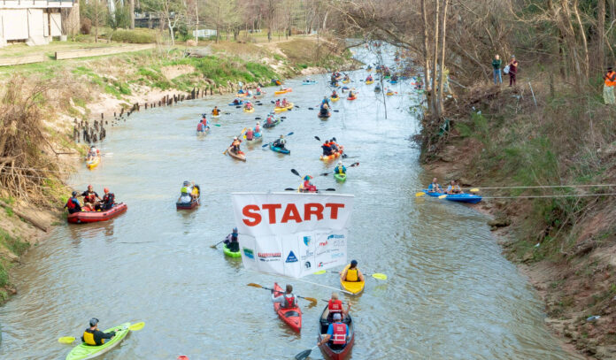 Paddlers in canoes and kayaks passing under a Starting Line