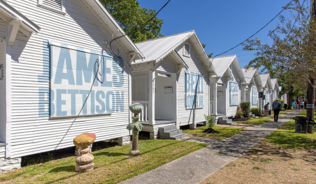 White shotgun-style houses in a row with light blue lettering that spells out the names of artists