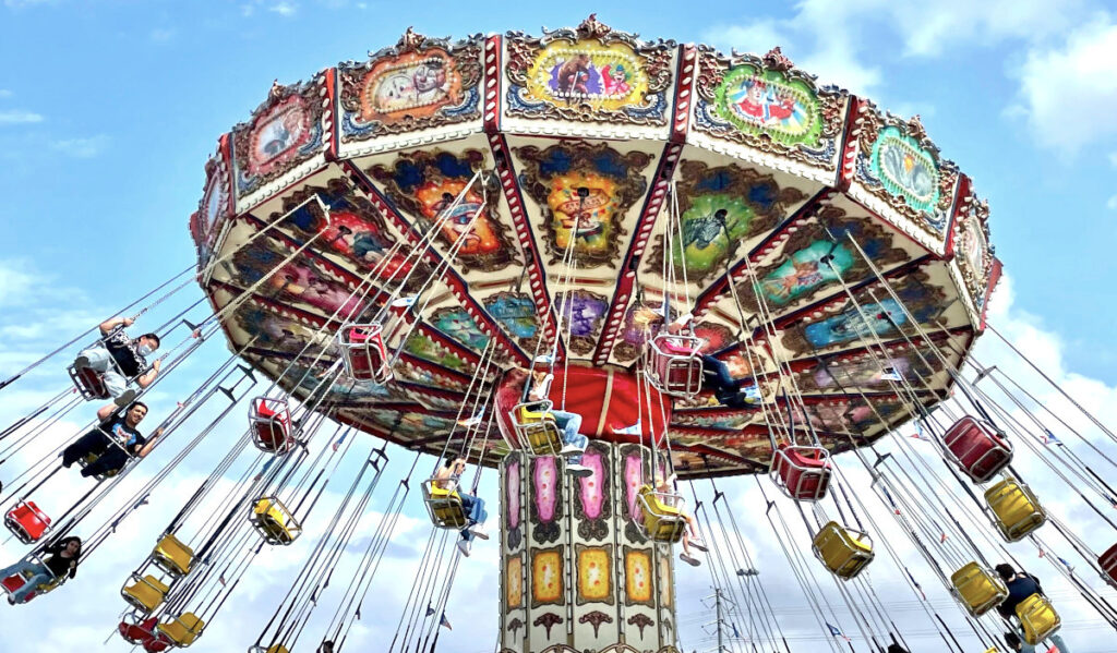 A carnival ride spins as people in bucket seats are hoisted into the air