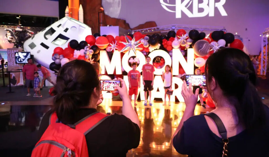 Three kids pose in front of letters saying "Moon 2 Mars"