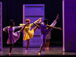 Three dancers on stage with a leg lifted high in purple and yellow light