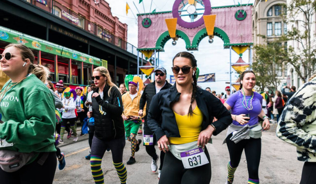 Runners in Mardi Gras-colored clothing running through a decorative arch in Galveston