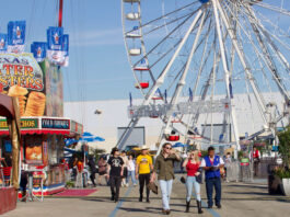 People walking past food stalls in western attire with a Ferris wheel behind them