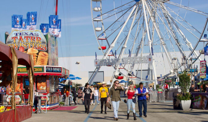 People walking past food stalls in western attire with a Ferris wheel behind them