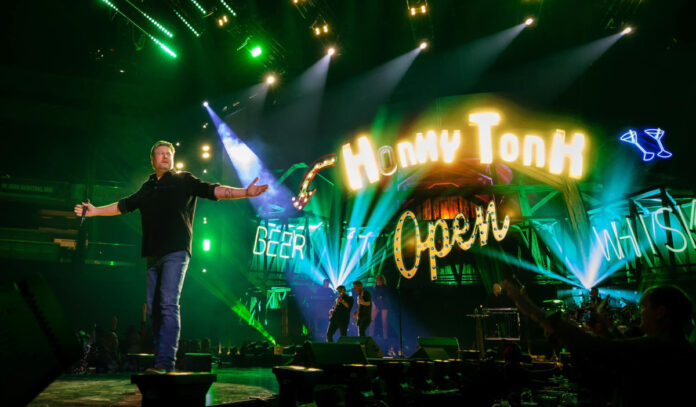 Blake Shelton standing on stage with his arms wide and a lit-up sign behind him that says Honky Tonk Open