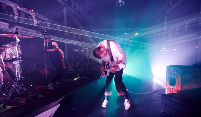 top-live-shows-concerts-in-houston-this-week-february-5-11-2024-portugal-the-man A guitarist bent over performing with a bright light shining behind him