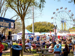 An outdoor carnival with festival goers eating and a Ferris Wheel in the background