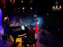 A performer in a red dress sings, accompanied by her band