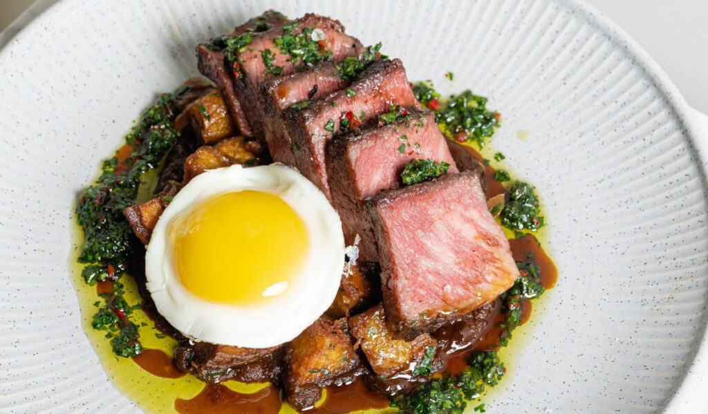 A plate of sliced meat with a chimichurri garnish and fried egg