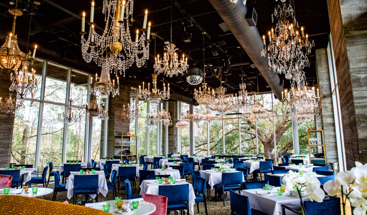 Brightly lit dining room interior with chandeliers and windows facing trees