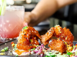 A plate of fried finger foods and a hand holding a pink and white drink in the background