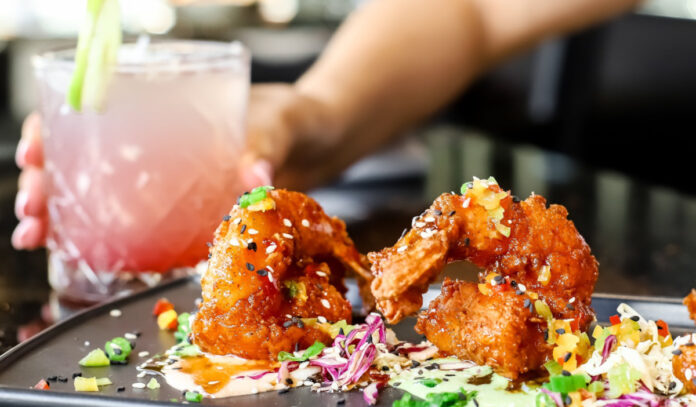 A plate of fried finger foods and a hand holding a pink and white drink in the background