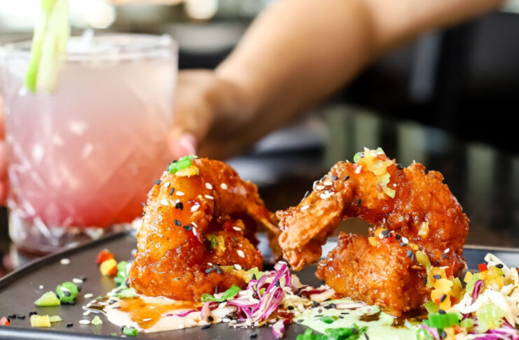 A plate of fried finger foods and a hand holding a pink and white drink in the background