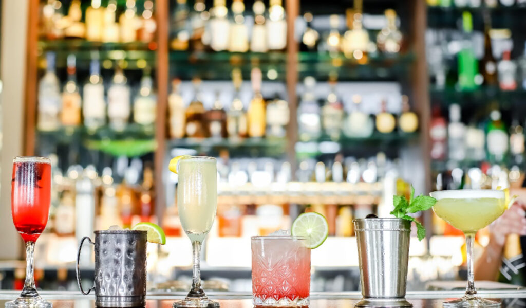 A lineup of six cocktails in various glasses sitting on a bar