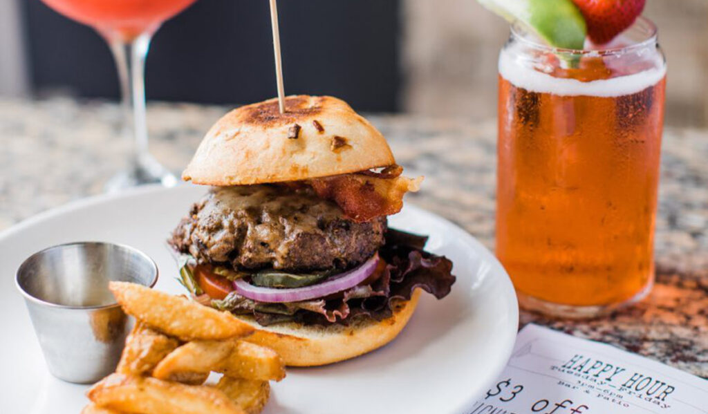 A burger and fries on a plate next to two cocktails 