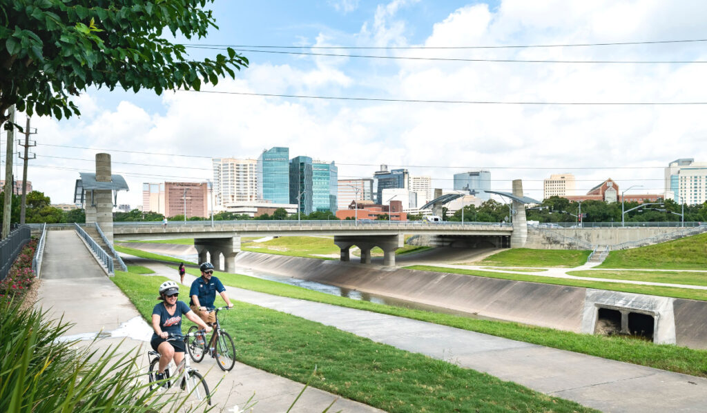 Two bicyclists riding down a path with a bridge and Medical Center buildings in the background