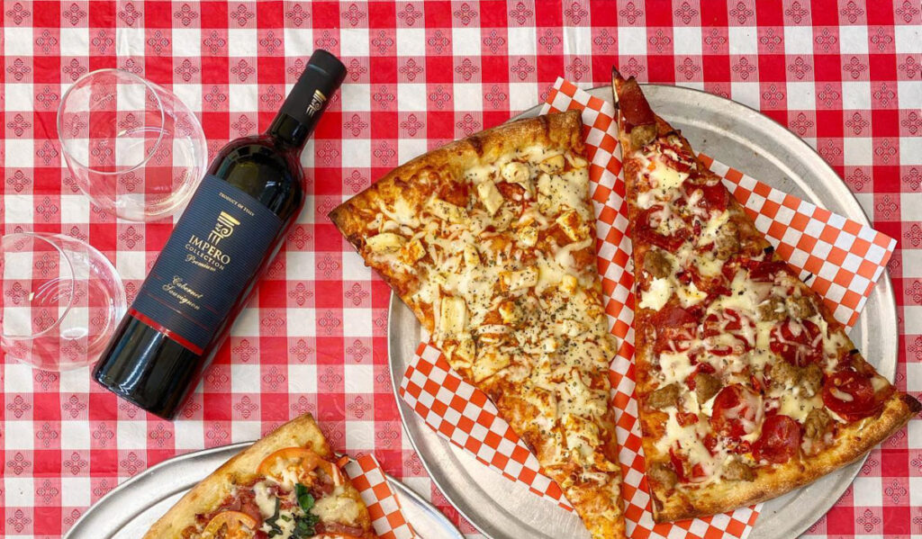 An overhead view of two large pizza slices next to a bottle of wine