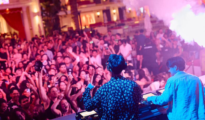 Two DJs performing for a crowd as a pyrotechnic goes off