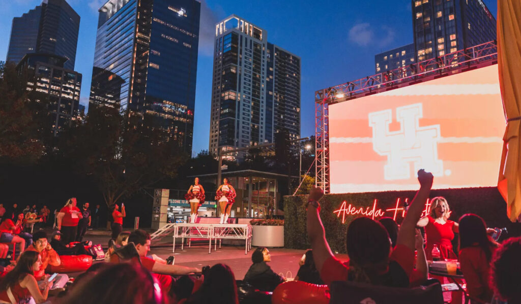 Fans watching a large screen at night with the Downtown Houston skyline