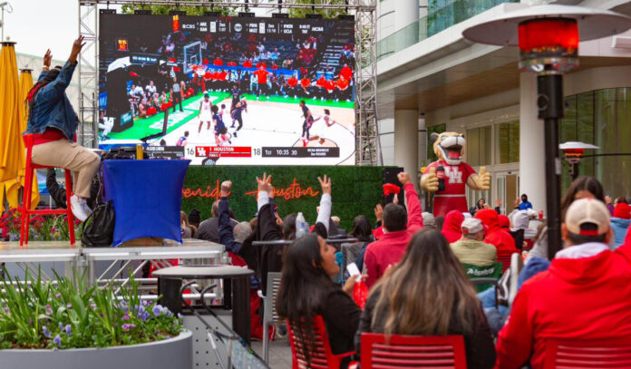 Fans celebrate on an outdoor patio while watching basketball on a big screen