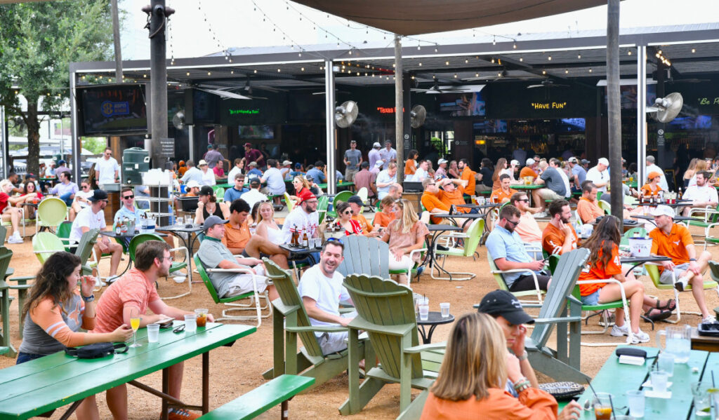 A spacious outdoor patio with fans in University of Texas clothes watching sports